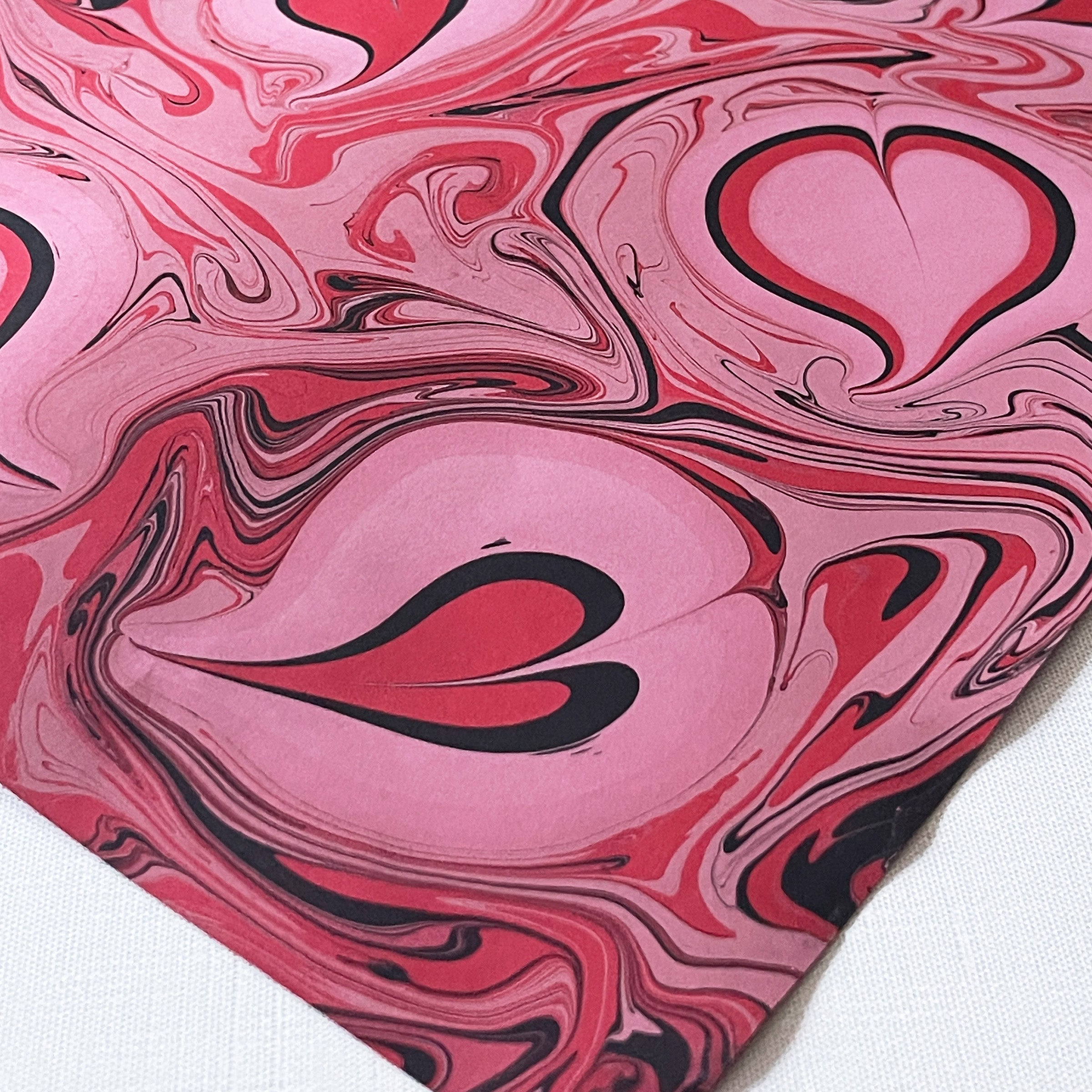 Detail of a marbled paper with pink, black, and pink swirls with marbled hearts