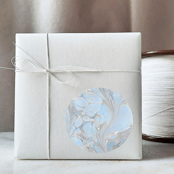 An elegantly wrapped gift adorned with a 3-inch round 'Aquatic Elegance' sticker, featuring a coordinating blue pattern, adding a touch of sophistication to the presentation. 
